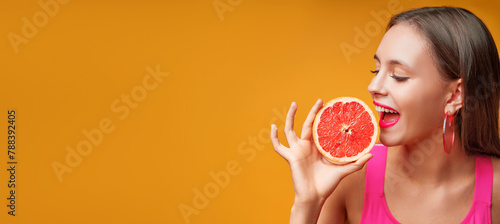 Beauty portrait of a lovely young woman with long hair standing over yellow background banner, showing slices of a grapefruit. © luengo_ua
