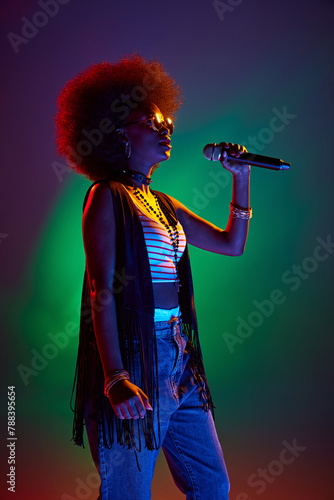 Portrait of young, attractive African-American woman singing in neon light against gradient background. Talent. Concept of art, music, hobby, classical music and modern lifestyle. Ad