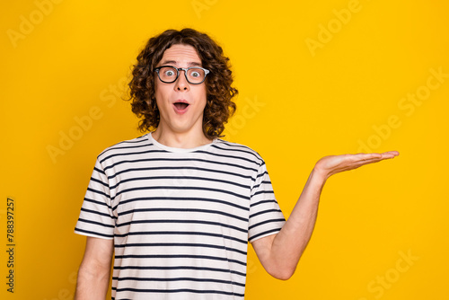 Photo portrait of nice teenager man excited shocked hand hold empty space wear trendy striped clothes isolated on yellow color background