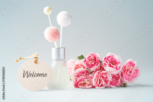 Fragrance diffuser with welcome tag and pink flowers on vintage blue background