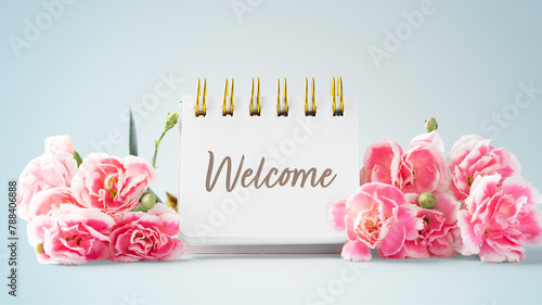 Welcome word on notepad and pink flowers on blue vintage background
