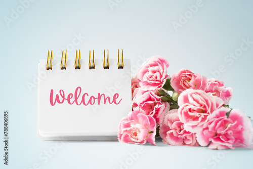 Welcome word on notebook and carnation flowers on blue vintage background