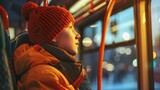 A boy in a red hat is sitting on a bus and looking out the window.