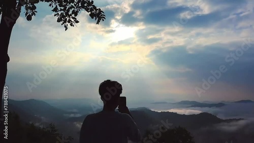 A person stands on a viewpoint and takes a video of the fog in Phu Bo Bit Forest Park, Loei Province, Thailand, and watches the sunrise. Miracles of nature hill standing shadow sunlight. - video photo