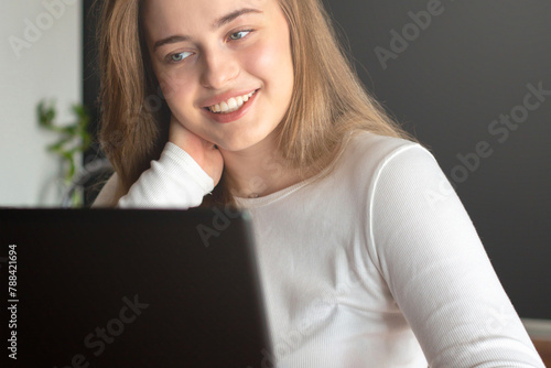 Close up a young smiling girl blonde with blue eyes that communicates on a laptop. Pastime and leisure at home.