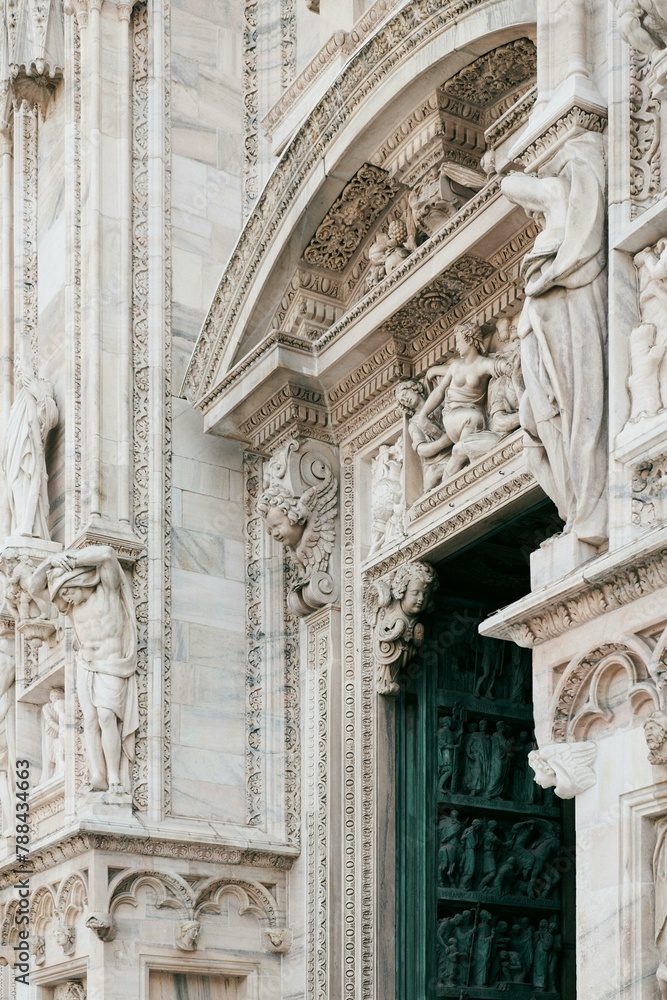 A close up of the facade of a building with a green door, showcasing medieval architecture and intricate relief sculptures. Columns and arches add to the monuments historic charm