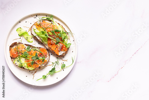 Homemade salmon sandwiches with fullgrain bread, pea micro greens, cream cheese and cucumbers on white marble background close up.