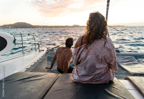 Rear View of Two People in a Catamaran Watching the Sunset Against a Coastal Horizon