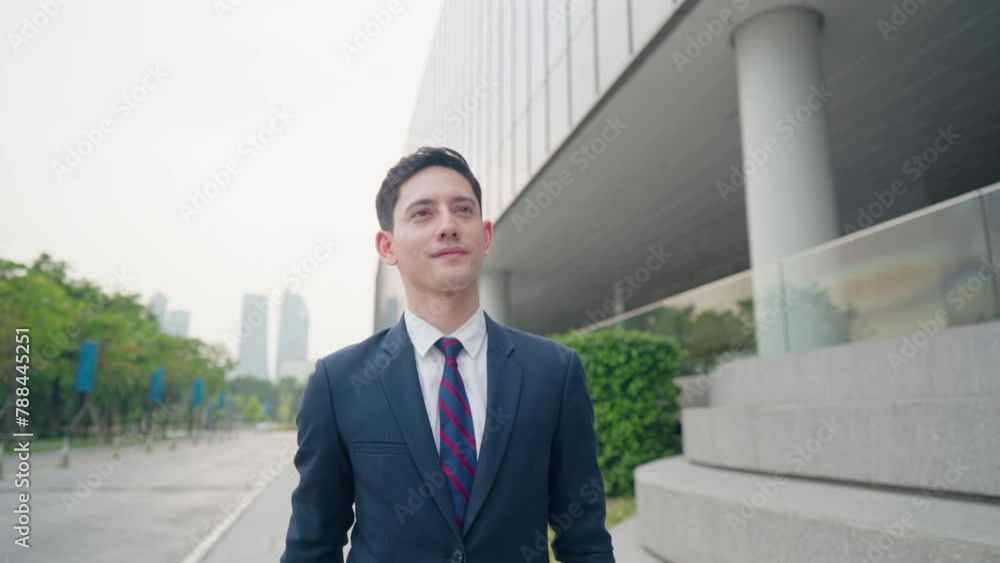 Shot of business working man walking along city walking path near glass office building with business briefcase, smart formal outfit, urban commuter walking along sidewalk, stop at look at the watch Shot of business working man walking along city walking path near glass office building with business briefcase, smart formal outfit, urban commuter walking along sidewalk, stop at look at the watch