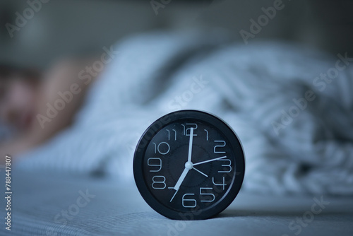 Alarm clock on bed. Kid boy teenager sleeping on the background.