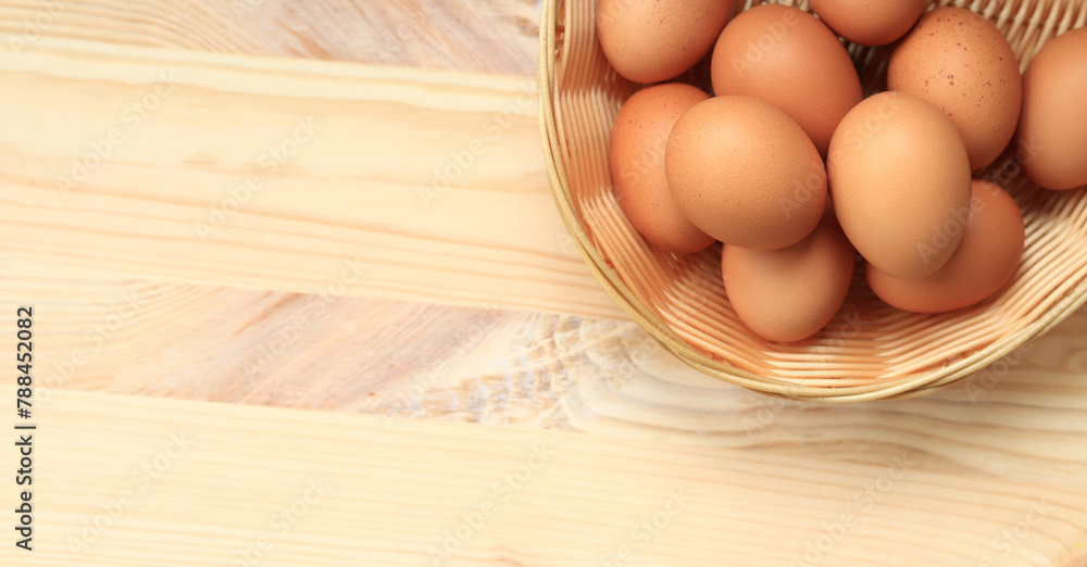 Chicken eggs in a wicker basket, top view. Eggs on a wooden background. Fresh raw eggs. Brown chicken eggs in a basket on a wooden table. Space for text - obrazy, fototapety, plakaty 
