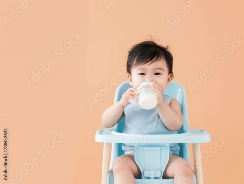 an Asian baby drinking milk on a high chair