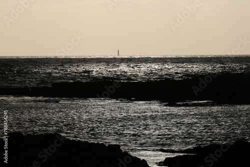 A small lighthouse on the horizon and a silver reflection on the Atlantic Ocean. Le Croisic, France - April 16, 2024.