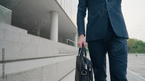 Mid Body shot of Businessman walking and look at wrist watch for the time, city walking path next to glass office building, smart formal clothes urban commuter, salesman going out for work photo