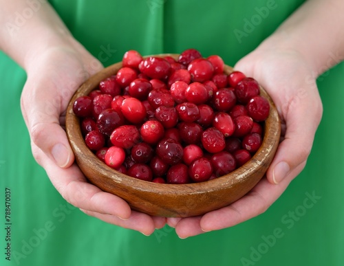 Woman holding wooden bowl full of frozen ripe cranberries in her hands. Close-up
