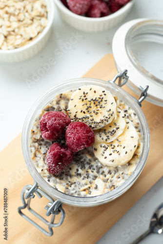 Overnight oats with chia seeds, bananas, raspberries, and plant-based milk in a jar for breakfast. Top view. Close-up. Healthy oatmeal pudding, eating organic vegan food concept.