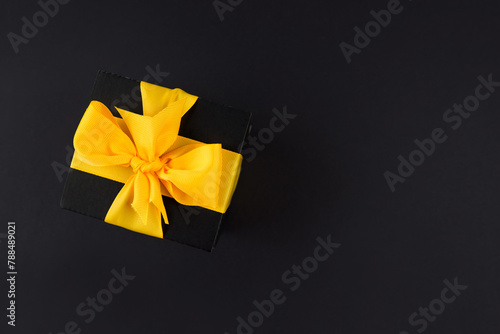 Top view photo of black gift box with ribbon wrapped as a bow isolated on black background