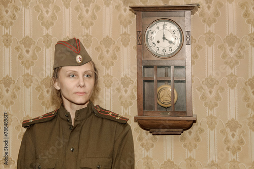 A woman in a military uniform against the background of old paper wallpaper and a clock with a pendulum.