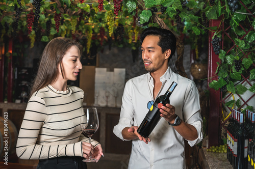 Wine seller man recommend good wine for young female customer in winery retail shop photo