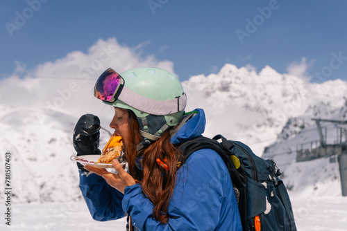 Woman skier snowboarder having lunch outdoors while skiing at ski resort in high mountains