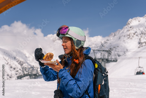 Woman skier snowboarder having lunch outdoors while skiing at ski resort in high mountains
