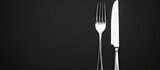 Close-up shot of a fork and knife against a black backdrop with room for text. Image has been toned.