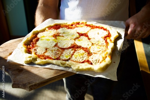 Male hands holding a cutting board with homemade pizza margherita