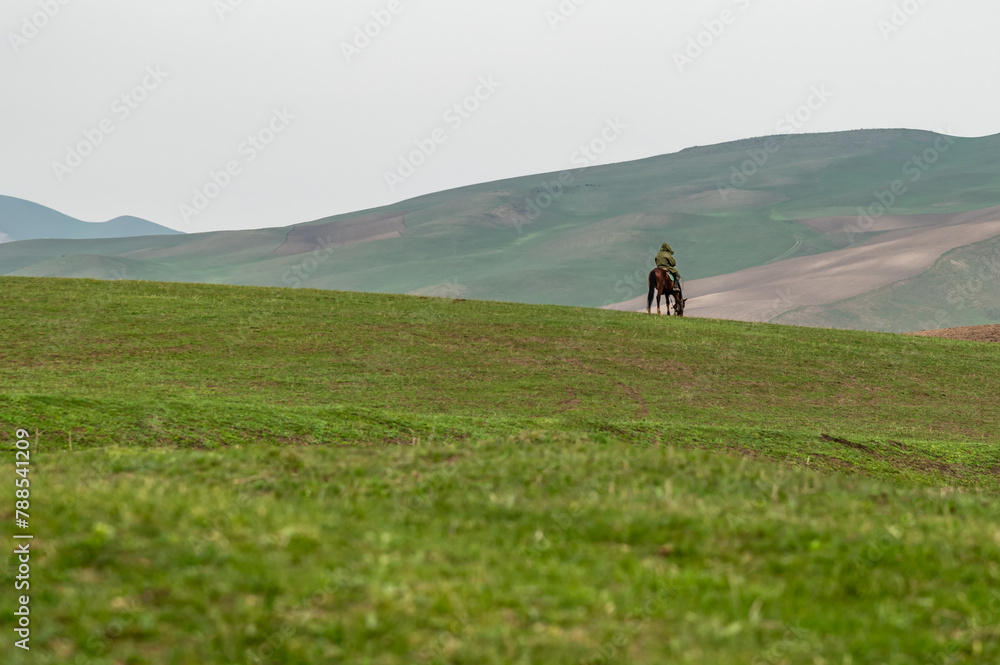 Lonely horseman on the green spring hills. Traditional life in the mountains of Kyrgyzstan.