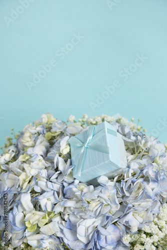 A gift box on a bouquet of hydrangea flowers on a blue background, space for text