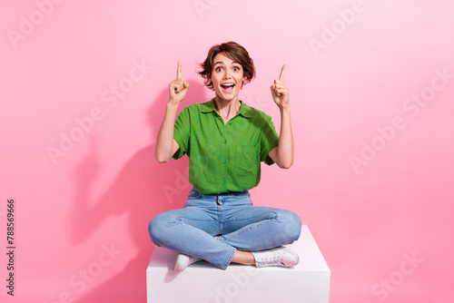 Full body photo of astonished pretty lady sit podium indicate fingers up empty space offer isolated on pink color background photo