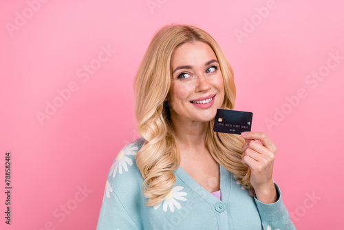 Portrait of cute person with curly hair wear blue cardigan hold credit card look at promo empty space isolated on pink color background