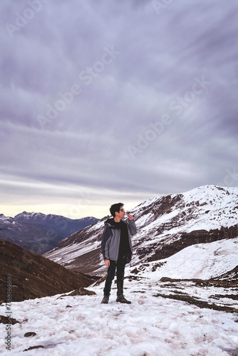 High altitude chill: young man enjoys a serene cannabis smoke from a pipe on a snowy mountain peak with panoramic views