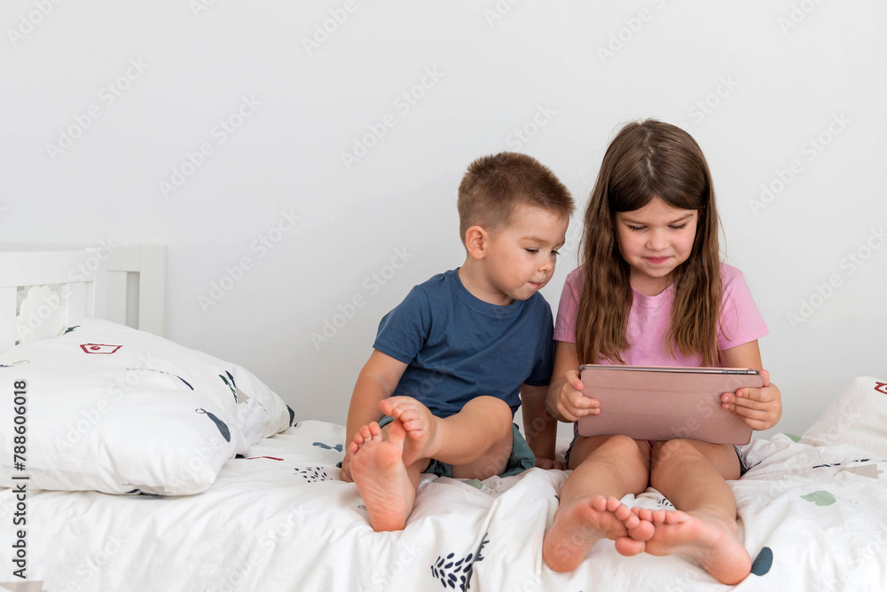 children sitting on the bed in the bedroom and looking at the tablet children sitting on the bed in the bedroom and looking at the tablet