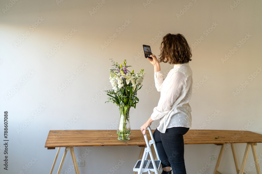 Woman taking photos flower arrangement on wooden table. Woman taking photos flower arrangement on wooden table.