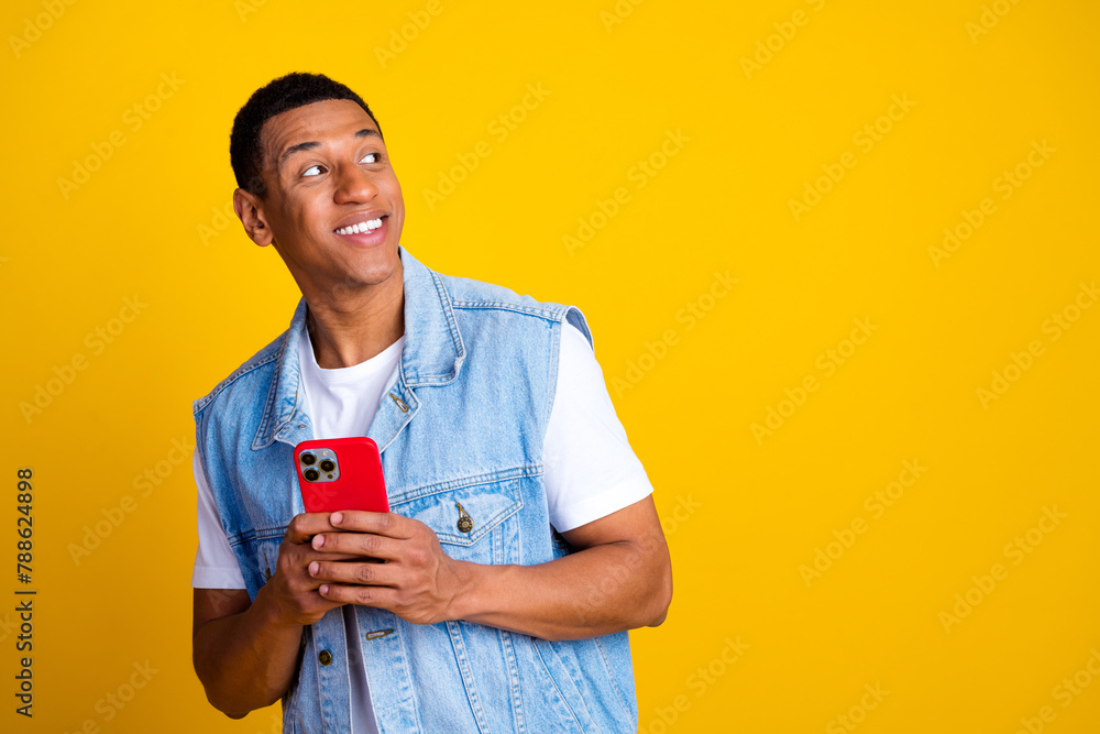 Photo of optimistic pleasant guy dressed jeans waistcoat hold smartphone look at offer empty space isolated on yellow color background Photo of optimistic pleasant guy dressed jeans waistcoat hold smartphone look at offer empty space isolated on yellow color background