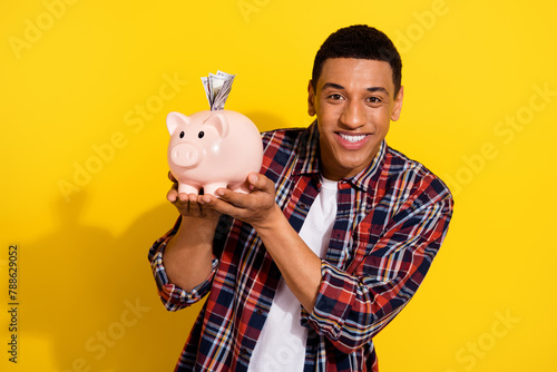 Photo of nice cheerful rich man wear stylish checkered clothes hold piggy bank money savings isolated on yellow color background photo