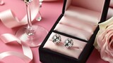 A pair of diamond stud earrings in a jewel box with a champagne glass and ribbon on a pink background