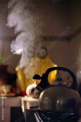 Tetera, pava o cafetera con vapor de agua hirviendo en la cocina en formato vertical