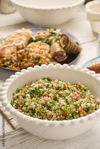 Fresh vegan Tabbouleh salad made of tomato, parsley, onion and couscous in bowl (Selective Focus, Focus one third into the salad) Other dishes arround