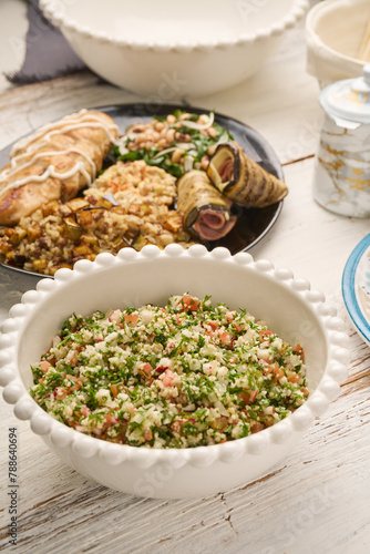 Fresh vegan Tabbouleh salad made of tomato, parsley, onion and couscous in bowl (Selective Focus, Focus one third into the salad) Other dishes arround