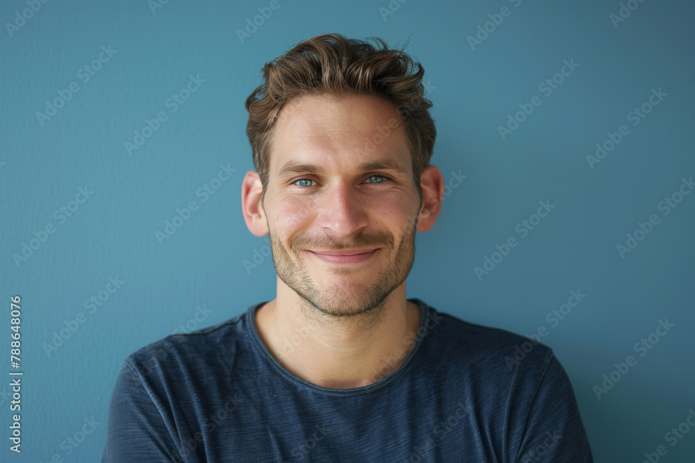 A man in a blue shirt is smiling in front of a blue wall A man in a blue shirt is smiling in front of a blue wall