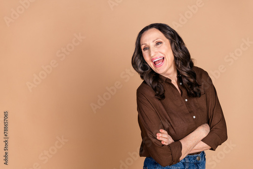Photo of attractive senior woman crossed hands confident look empty space dressed stylish brown clothes isolated on beige color background