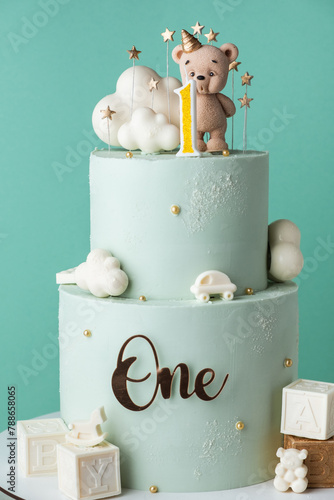 Two tier birthday cake for a little kid with turquoise chocolate frosting. Birthday cake for a one year old baby decorated with chocolate teddy bear figurine and clouds