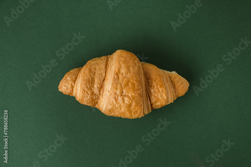 Flat lay of single freshly baked croissant on the green background. Traditional French pastry with a copy space for a free text