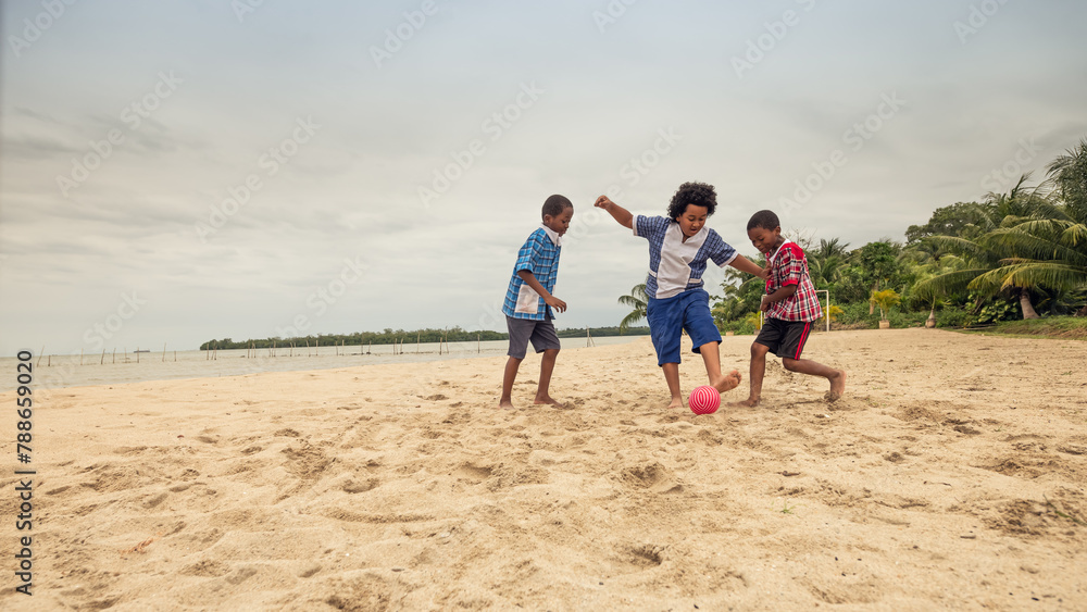 Three boys compete for the ball in a soccer game on a beach.