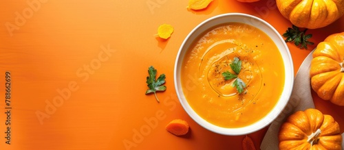 Pumpkin soup displayed on a vibrant orange backdrop. Freshly made pumpkin soup served in a clean white bowl. Flavorsome mixture of pumpkin and carrot soup. Ample space for text.