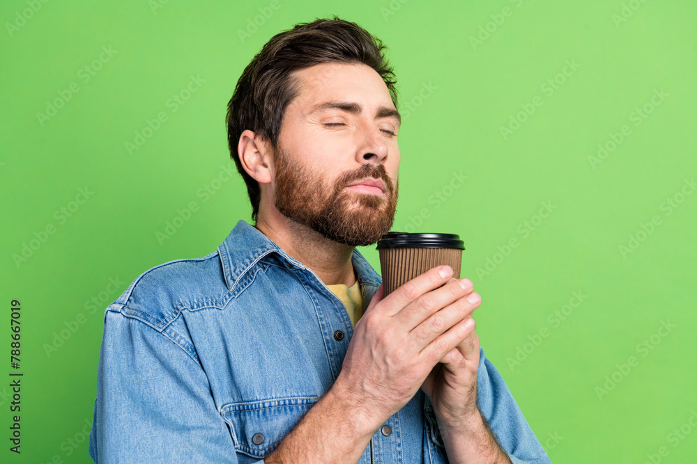 Photo of good mood dreamy guy wear denim jacket enjoying coffee closed eyes empty space isolated green color background Photo of good mood dreamy guy wear denim jacket enjoying coffee closed eyes empty space isolated green color background