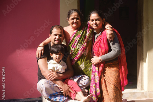 Portrait of a south asian hindu religious family sitting together in front of a door in a sunny day