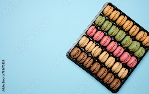 Multi-colored macarons on a blue background in a plastic box  top view