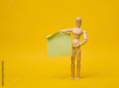 Wooden puppet puppet holding blank sticker sheet on yellow background